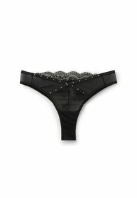 Tanga de encaje negro con borde superior con forma de ondas y tachuelas decorativas. Fabricada en malla transparente con patrones florales y cinturilla elástica.