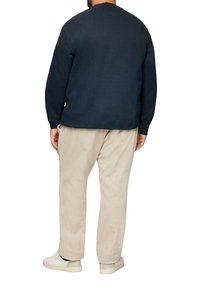 Sweatshirt à col rond bleu marine, pantalon en velours côtelé beige, baskets blanches. Design sobre avec une finition texturée ; détails de couture subtils visibles.