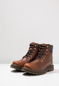 Botas de cuero marrón con diseño de cordones, ojales dorados y suela resistente con un diseño de dibujo. Cuello suave para mayor comodidad.
