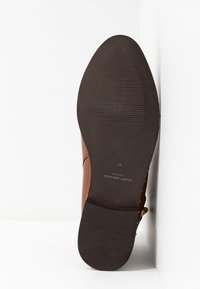Suela de zapato de cuero marrón con fondo de goma negra texturizada, tamaño 37, marca "Kurt Geiger London" visible en texto blanco.