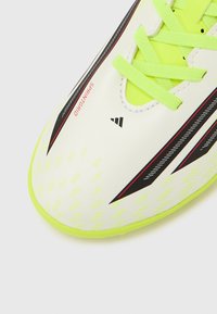 Κοντινό πλάνο ενός αθλητικού  παπουτσιού Adidas σε νέον κίτρινο και λευκό με μαύρες και κόκκινες λεπτομέρειες και το κείμενο «SPRINTGRIP» κοντά στα δάχτυλα.