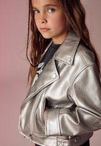 Silverfärgad faux läderjacka med en kort, figurnära design, som har dragkedja och sidofickor. Texturerad yta och slagkrage.