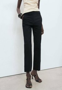 Pantalons noirs ajustés avec une coupe droite, fabriqués à partir d'un tissu lisse. Associés à des sandales à talons hauts noires minimalistes.