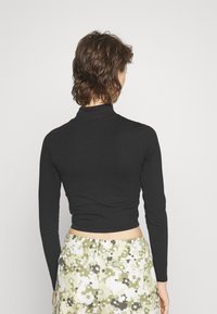 Svart tajt långärmad polotröja kombinerad med mönstrade kamouflageshorts i grönt, vitt och svart, med bakfickor.