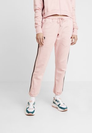 Pantalones de chándal rosa con franjas laterales negras, que cuentan con una cinturilla elástica y puños. Combinados con zapatillas multicolores.