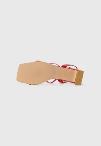 Sandale à talon rouge avec un bloc de talon beige carré, des fines lanières et une semelle lisse avec une texture rainurée.