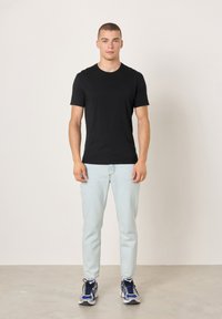 Crna majica kratkih rukava s okruglim izrezom; uparen s svijetloplavim trapericama i višebojnim tenisicama za trčanje s tamnim vezicama.