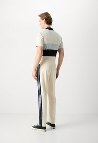 Polo majica v svetlo bež barvi z sivo in črnima vodoravnima črtama; v kombinaciji z bež hlačami, ki imajo modre stranske črte in črne čevlje.
