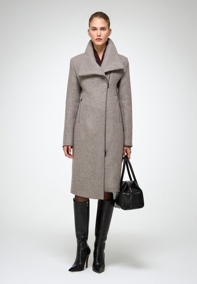 Cappotto lungo grigio in lana con colletto alto, tasche laterali e zip frontale; abbinato a stivali neri in pelle fino al ginocchio e una borsa nera.