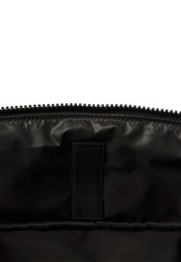 Interior de una bolsa negra de nailon con cierre de cremallera, que presenta una textura suave y lisa, y un lazo de tela para un fácil transporte o sujeción.