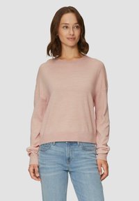 Lichtroze trui met lange mouwen, een ronde hals en een geribbelde onderkant. Zachte textuur, losse pasvorm, gecombineerd met lichtblauwe jeans.