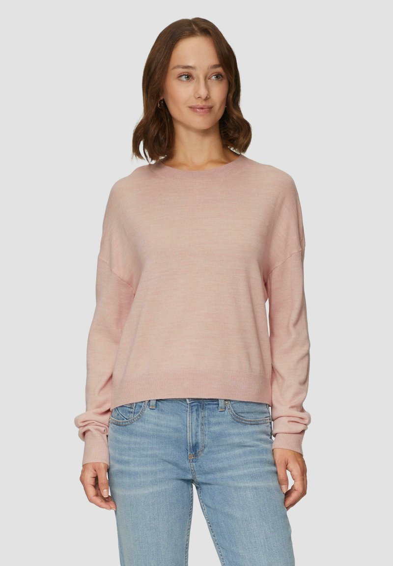 Lichtroze trui met lange mouwen, een ronde hals en een geribbelde onderkant. Zachte textuur, losse pasvorm, gecombineerd met lichtblauwe jeans.