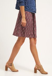 Sukně s květinovým vzorem v burgundské barvě se modrými a zelenými akcenty, doplněná tanovými sandály na bloku s otevřenou špičkou a džínovou bundou.