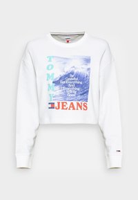 Sweatshirt court blanc en coton. Présente un graphique d'onde bleue avec le texte : "Soyez reconnaissant pour tout" et "TOMMY JEANS" en orange et turquoise.