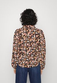 Blusa floreale con sfondo nero, caratterizzata da fiori arancioni e crema, maniche lunghe e colletto.