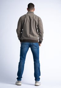 Šedá bomber bunda s stojáčkem, žebrovanými manžetami a hladkým povrchem, spárovaná s modrými džíny a bílými teniskami.