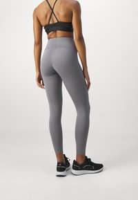 Leggings grigi alti in vita con una texture liscia, abbinati a un reggiseno sportivo nero e scarpe da ginnastica nere con suole bianche.