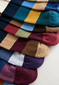 Kolorowe skarpetki ułożone w wachlarz, z paskami w odcieniach niebieskiego, zielonego, żółtego, brązowego i bordo. Widoczna dzianinowa faktura.