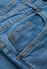 Tissu en denim de couleur bleue, avec des coutures orange et un petit détail de poche. La texture semble douce et résistante.