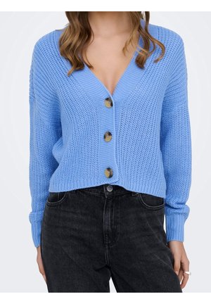 Cardigan en maille bleu clair à boutons avec trois boutons marron, porté avec un jean noir taille haute et une bague argentée à la main droite.