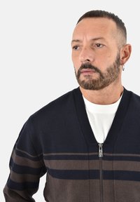 Cardigan a righe blu navy e marrone con zip frontale, realizzato in morbido tessuto a maglia, con scollo a V e righe strutturate.