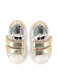 Des baskets pour enfants avec accents dorés présentent un corps en synthétique blanc, deux straps Velcro réglables, et un graphique de dessin animé sur la semelle intérieure.