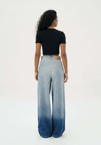 Zwarte cropped t-shirt gecombineerd met high-waisted, wijde jeans met een verloop van licht naar donkerblauw en achterzakken.