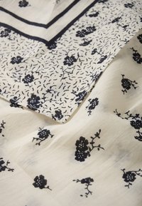 Tessuto di cotone con sfondo bianco, caratterizzato da un motivo floreale blu navy e un delicato disegno a linee. Texture morbida e leggero.