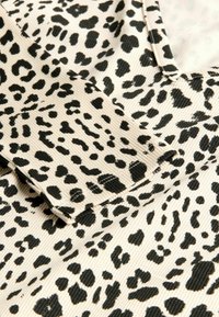 Tessuto animalier in beige e nero, con una texture a coste e cuciture a contrasto. Dettaglio ravvicinato del colletto e della manica.