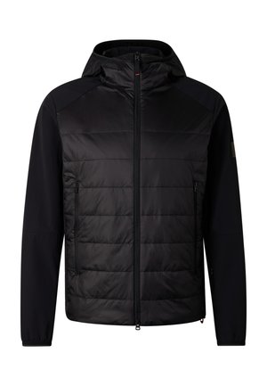 Mann trägt schwarze Steppjacke mit Kapuze, schwarze Jogginghose, schwarze Mütze, reflektierende Sonnenbrille und schwarze Sneakers, steht vor weißem Hintergrund.