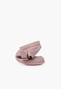Zapato de cuero suave color rosa, con una silueta flexible y una correa ajustable, que presenta una textura lisa y un diseño de punta redondeada.