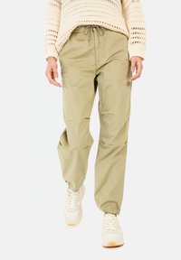 Khakifarbene Jogginghosen mit elastischem Bund, Kordelzug und schmal zulaufendem Bein. Kombiniert mit beigen Sneakers, die strukturierte Strickdetails aufweisen.