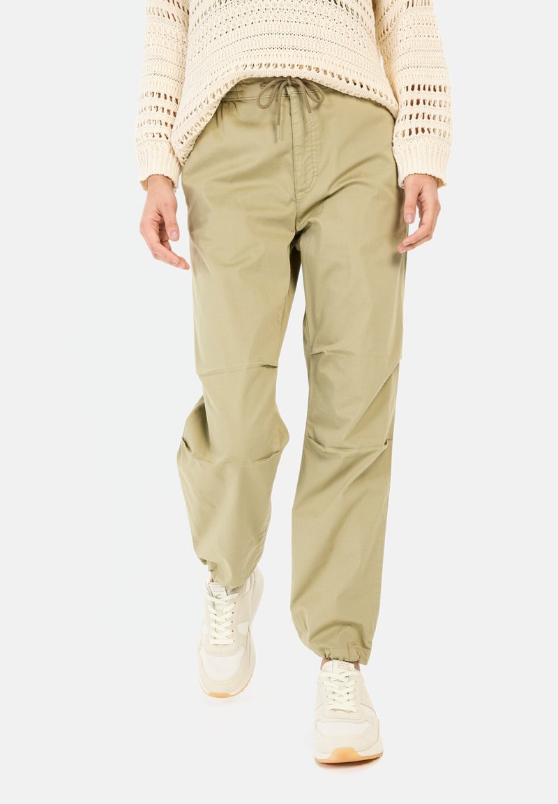 Khakifarbene Jogginghosen mit elastischem Bund, Kordelzug und schmal zulaufendem Bein. Kombiniert mit beigen Sneakers, die strukturierte Strickdetails aufweisen.