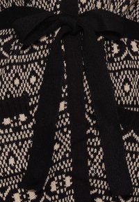 Strickcardigan in Schwarz und Creme mit geometrischen Mustern, ausgestattet mit einem gebundenen Gürtel und vorderen Taschen. Strukturierter Stoff mit gerippten Akzenten.