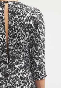 Svart och vitmönstrad klänning med rund halsringning, trekvartslånga ärmar och en nyckelhålsdetalj i ryggen. Slät tygtextur.