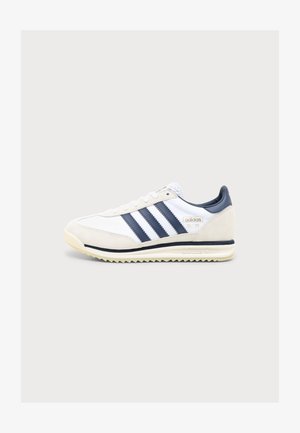 Baskets Adidas SL 72 blanches et beiges avec des bandes noires et une semelle texturée, vues de côté sur un fond gris clair.