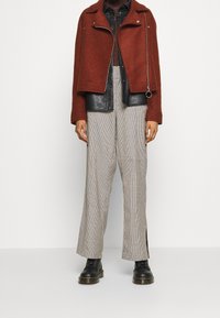 Giacca in misto lana marrone con dettagli in pelle nera, pantaloni a scacchi a vita alta e stivali neri con lacci; dettagli hardware minimi sulla giacca.
