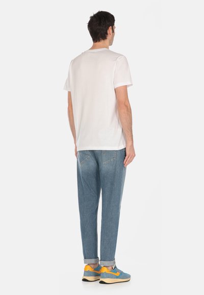 T-shirt bianco in cotone con maniche corte, abbinato a pantaloni in denim azzurro. Il modello indossa sneakers blu e gialle. Fit casual e linee pulite.