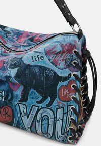 Denim-Handtasche mit schwarzer Katzen-Grafik, Graffiti-ähnlichem Text und schwarzem Schnürdetail an der Seite mit silbernen Ösen und Reißverschluss.