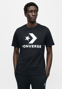 Μαύρο βαμβακερό t-shirt με μεγάλο λευκό λογότυπο Converse που περιλαμβάνει σχέδιο αστέρι και βέλος στο μπροστινό μέρος. Λαιμόκοψη τύπου crew, κοντά μανίκια.