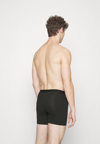 Black boxer shorts made of soft fabric, featuring a smooth waistband. The model is seen from behind, with a light skin tone and curly hair.