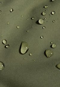 Waterafstotende olijfgroene stof met een gestructureerd oppervlak, met verschillende maten waterdruppels die erop liggen.