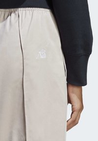 Beiga träningsbyxor med elastisk midja och en synlig vit broderad logotyp. Texturerat tyg med en slät yta, sid sömsdetalj.