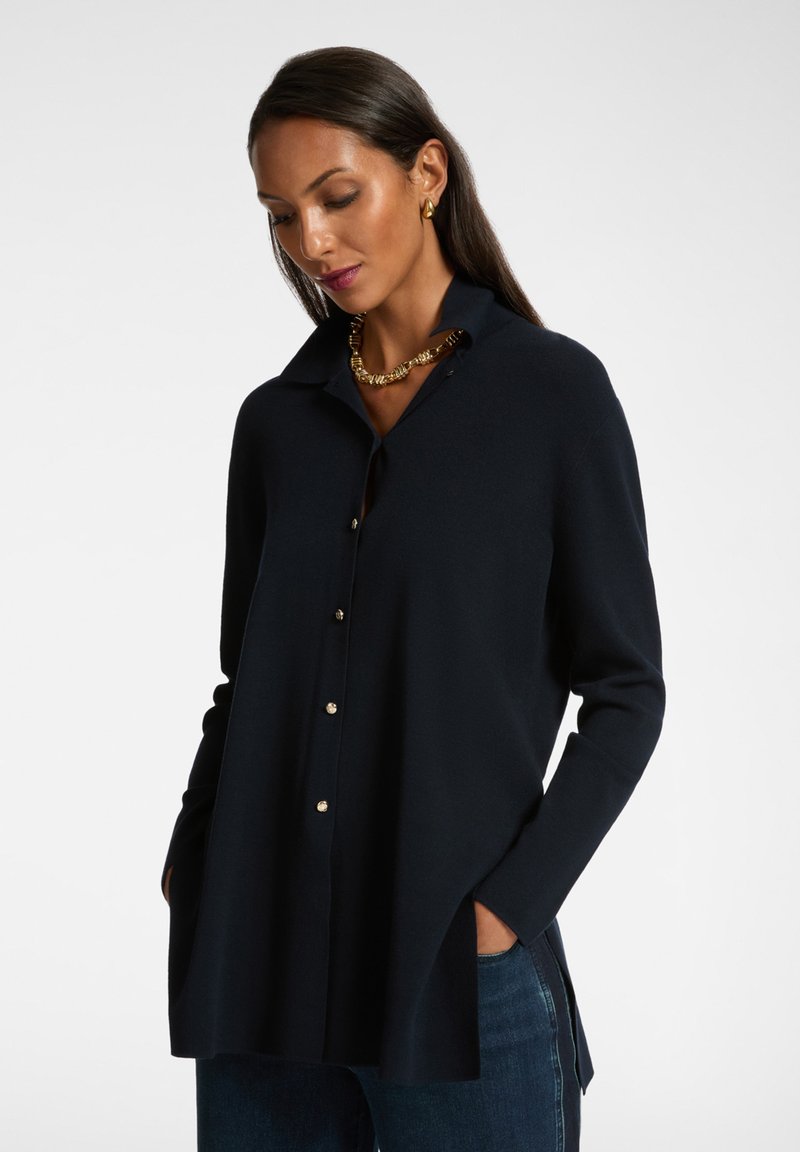 Blusa de manga larga color navy hecha de una tela suave, con un cierre frontal de botones, botones dorados, aberturas laterales y un diseño clásico de cuello.