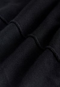 Krupni plan presavijenog crnog pletenog tkanja koji prikazuje teksturirani vez i ušivene šavove.