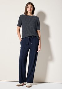 Navy wijde broek met een drawstring taille en zijstrepen, gecombineerd met een textuur navy t-shirt met korte mouwen. Casual sneakers maken de look compleet.