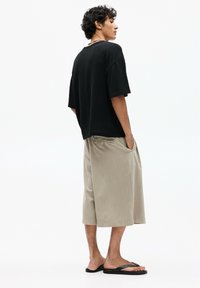 T-shirt noir surdimensionné et shorts beiges arrivant aux genoux, assortis de tongs noires. Le T-shirt est en tissu texturé ; les shorts disposent de poches latérales.