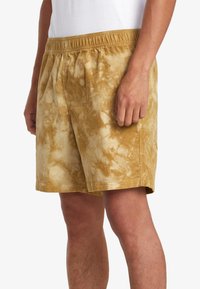 Tan corduroy shorts with a tie-dye effect, featuring an elastic waistband and side pockets, mid-length, and a soft, textured surface.
