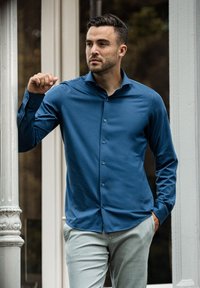 Langsleeve, knoopshirt in diepblauw, gemaakt van een gladde stof, met een vrij scherpe kraag en subtiele knoopaccenten, gedragen met lichte broek.