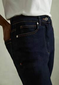 Mörka denimjeans med orange sömmar, femficksdesign och metalldragkedja. Klassisk passform med en mjuk textur.